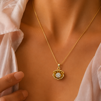 A close-up of a model wearing a delicate gold chain necklace with a small, flower-shaped gold pendant featuring a clear central gemstone, styled with a soft white blouse.